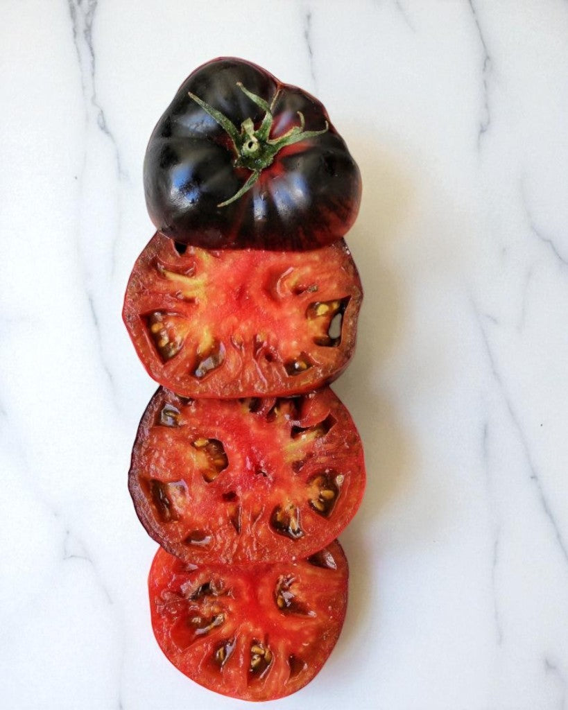 Whole and sliced Black Beauty tomato on a white marble surface