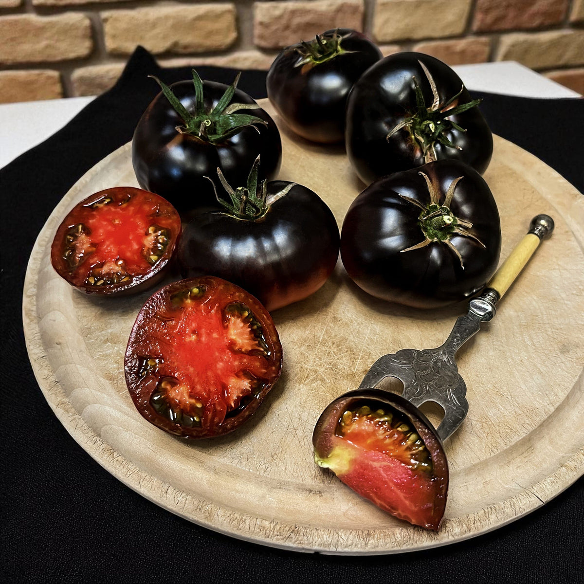 Black Beauty tomatoes on a wooden board with a brick wall background
