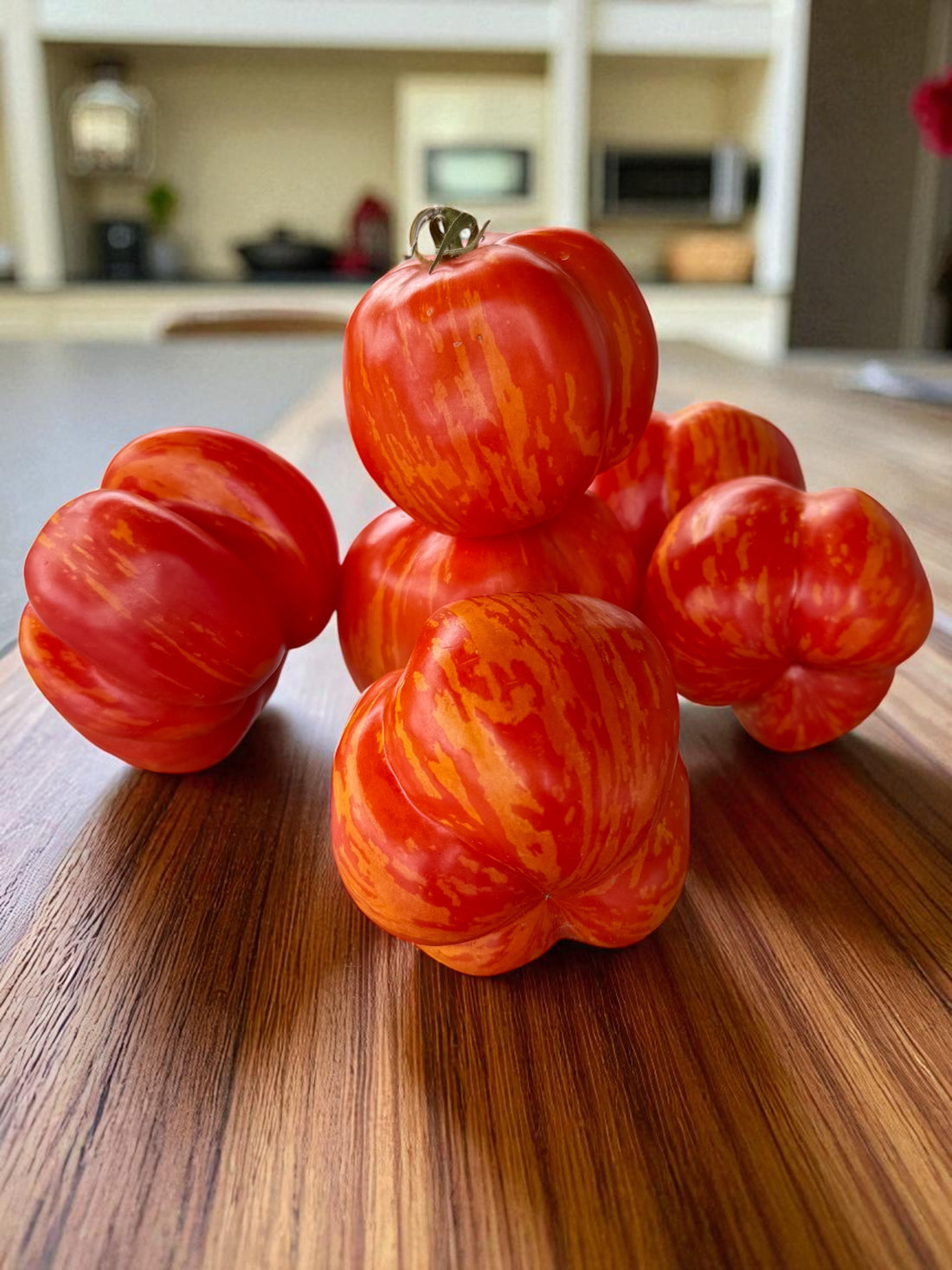 Red and orange marbled Charlie Chaplin tomatoes on a wooden surface with a kitchen background